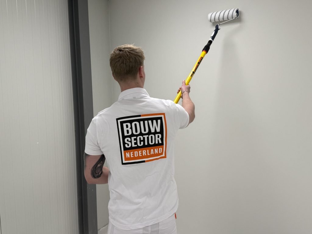 Schilder met getatoeëerde arm rolt een lichte wand hoog bij het plafond in een smalle ruimte
