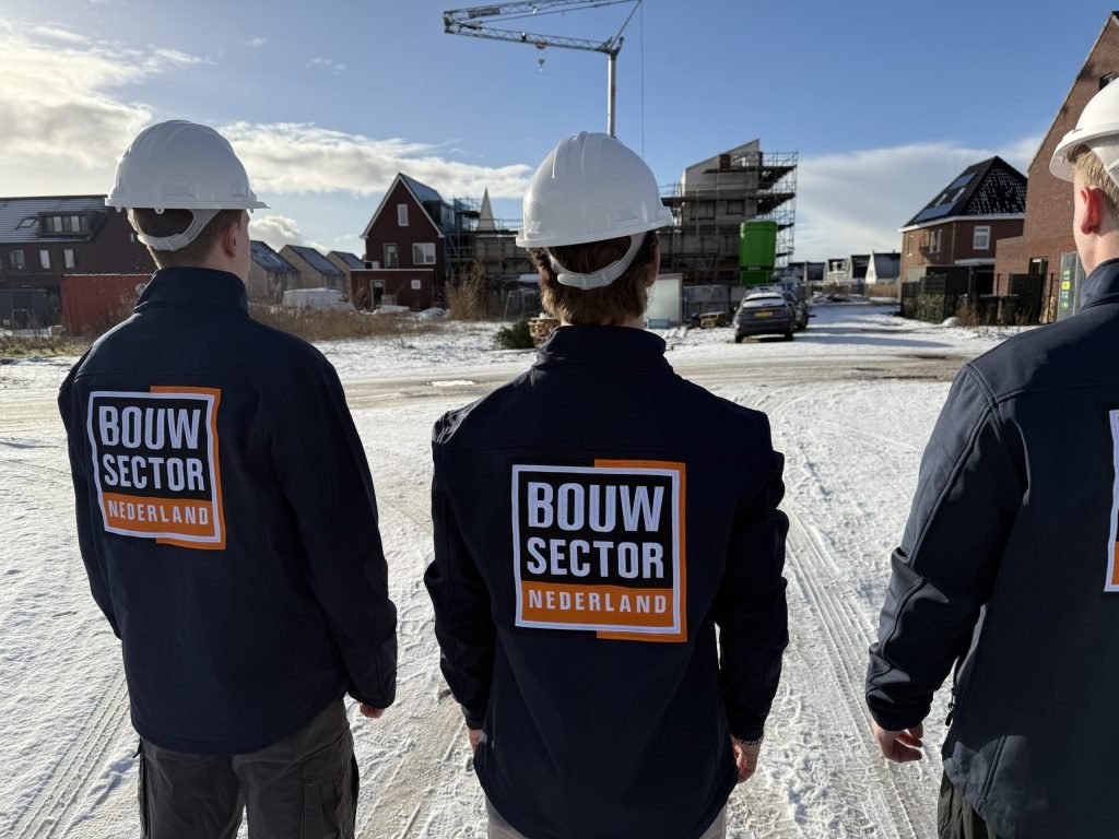 Drie vakmensen van Bouwsector Nederland met witte helm kijken naar nieuwbouwhuizen in aanbouw